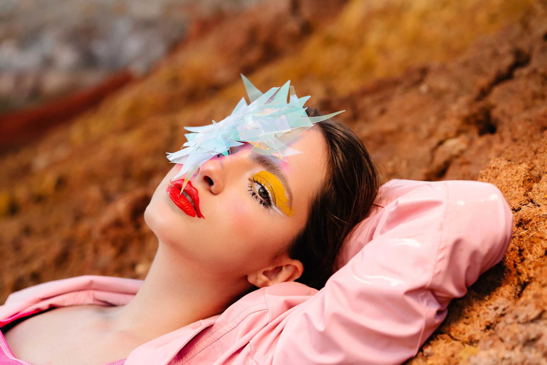 A striking portrait of a model with vibrant makeup and futuristic elements on rugged terrain.