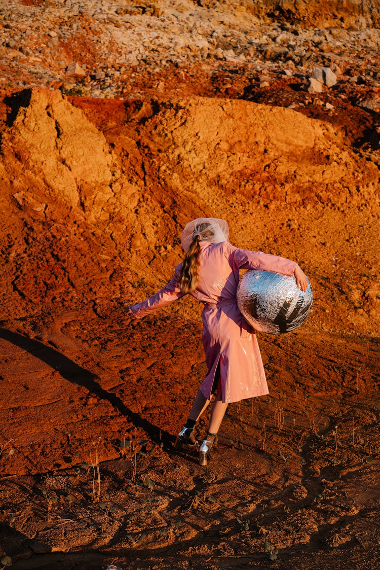 Back View Of A Woman In A Coat And High Heels Walking With A Silver Ball