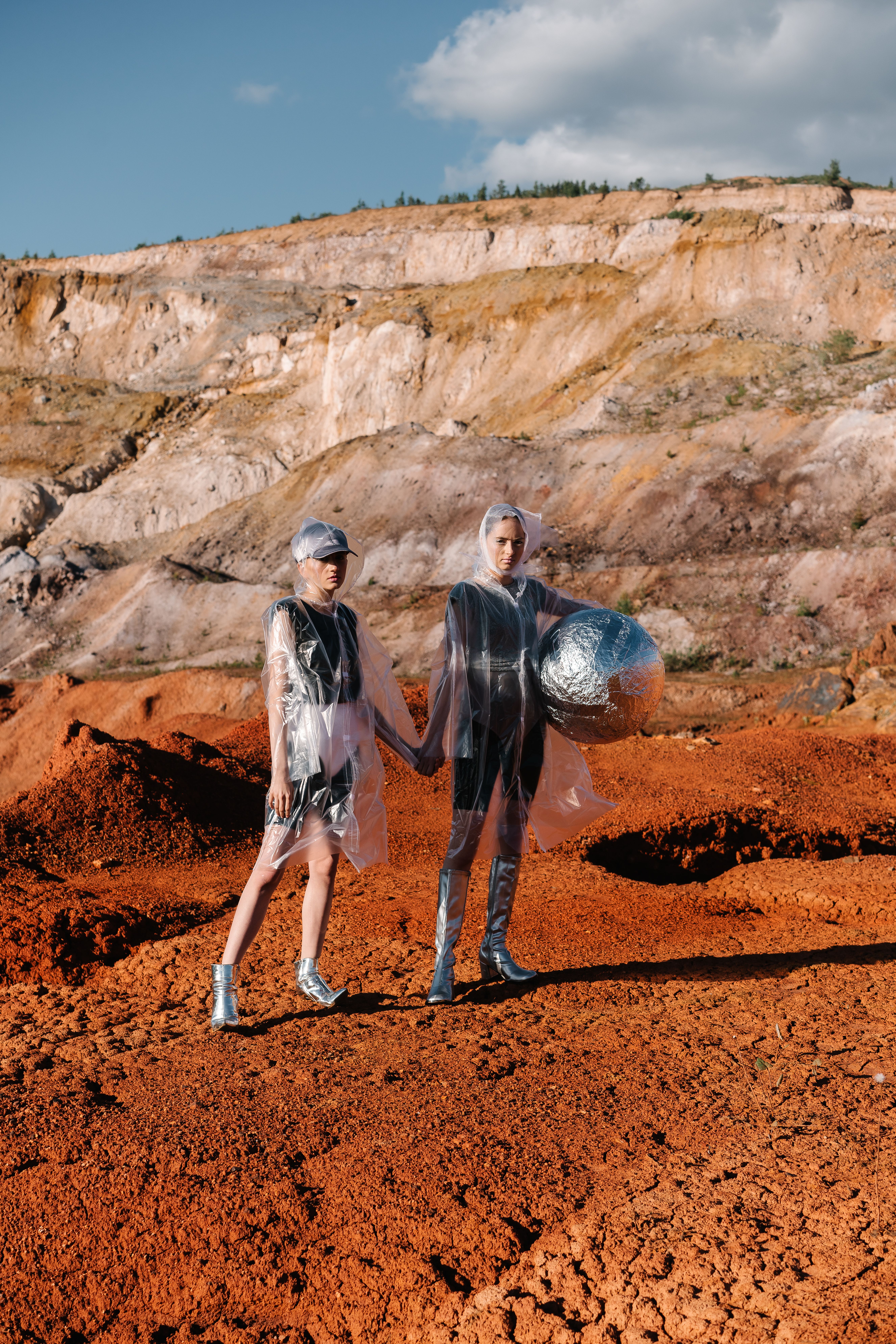 Models in avant-garde outfits holding hands in a desert setting. Unique fashion photography.