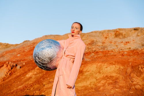 A Woman in Coat Posing with a Silver Ball