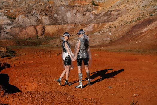 Two Women Holding Hands While Walking on Red Sand