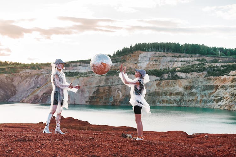 Women In Transparent Raincoats Throwing A Ball Covered With Foil