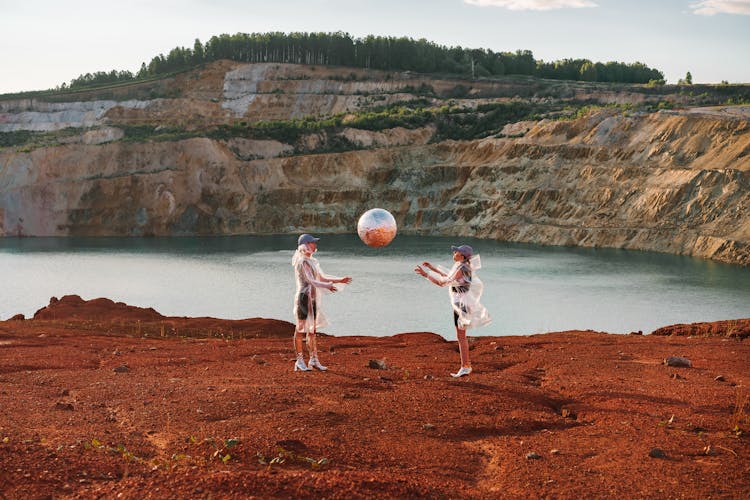 Women In Transparent Raincoats Throwing A Ball Covered With Foil