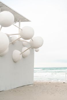 Modern white spherical sculptures adorn a beachside building by the calm sea.