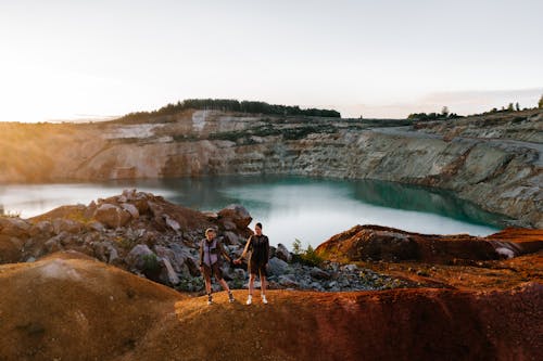 Women in Mesh Dressed Holding Hands on Red Stone by a Lake