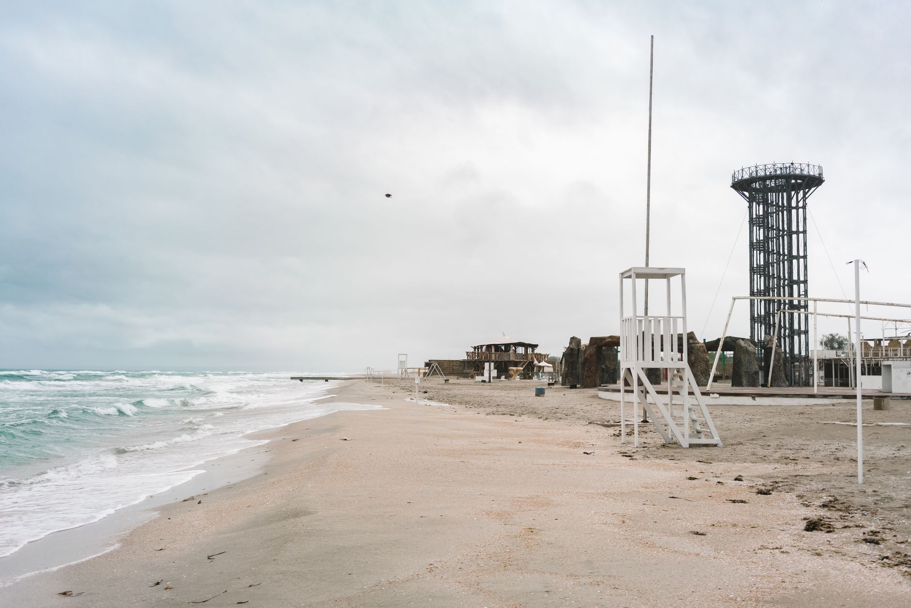 A tranquil ocean view of a sandy beach with unique structures and a cloudy sky.