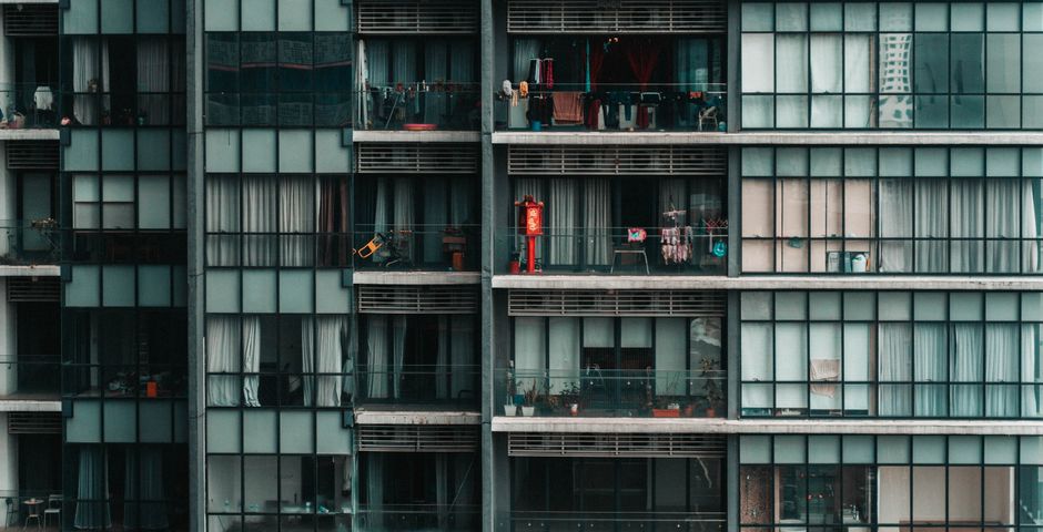 Facade of a modern apartment building with stacked balconies — units share continuous plumbing and service risers