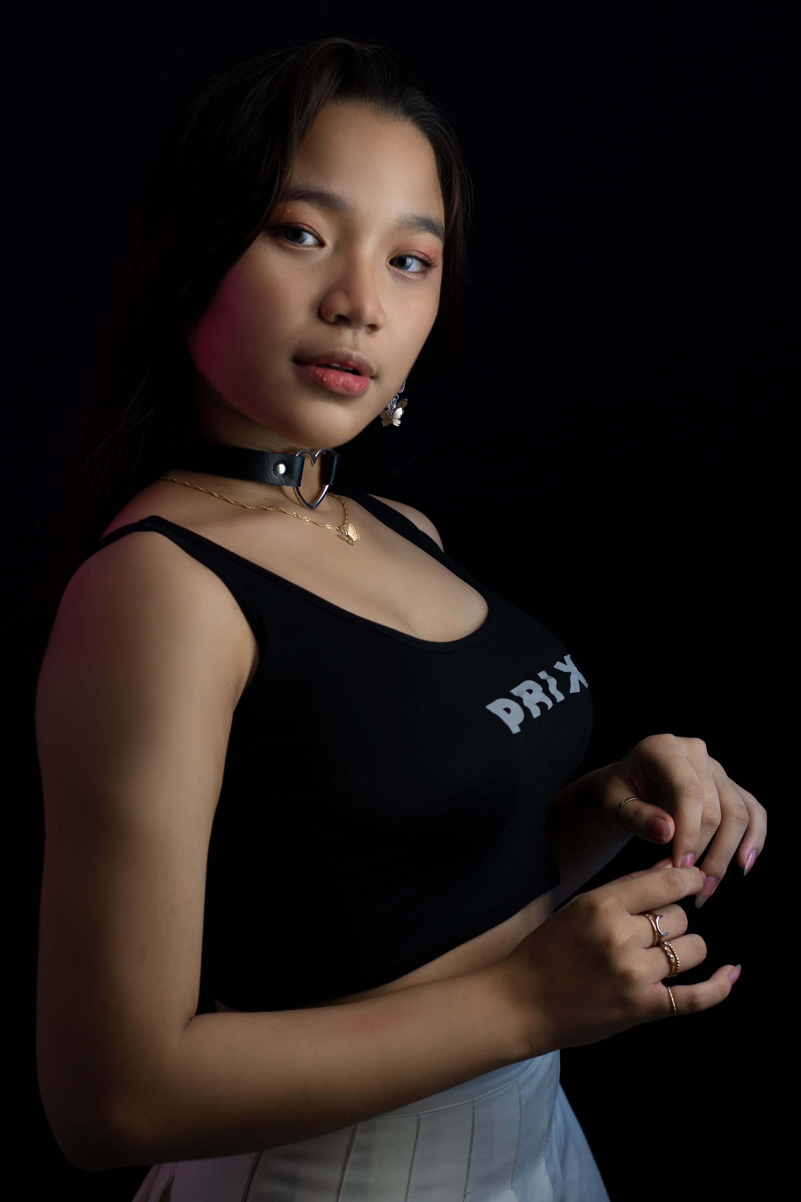 A fashionable Asian woman posing confidently in a black tank top against a dark backdrop.