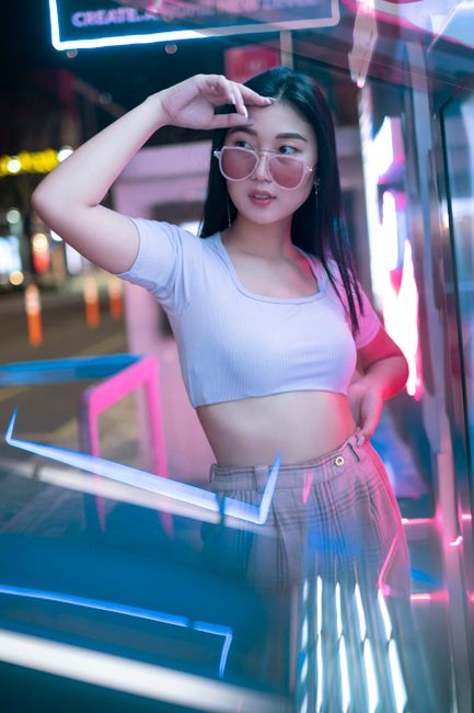 Stylish young woman poses with neon lighting in an urban setting, showcasing modern fashion.