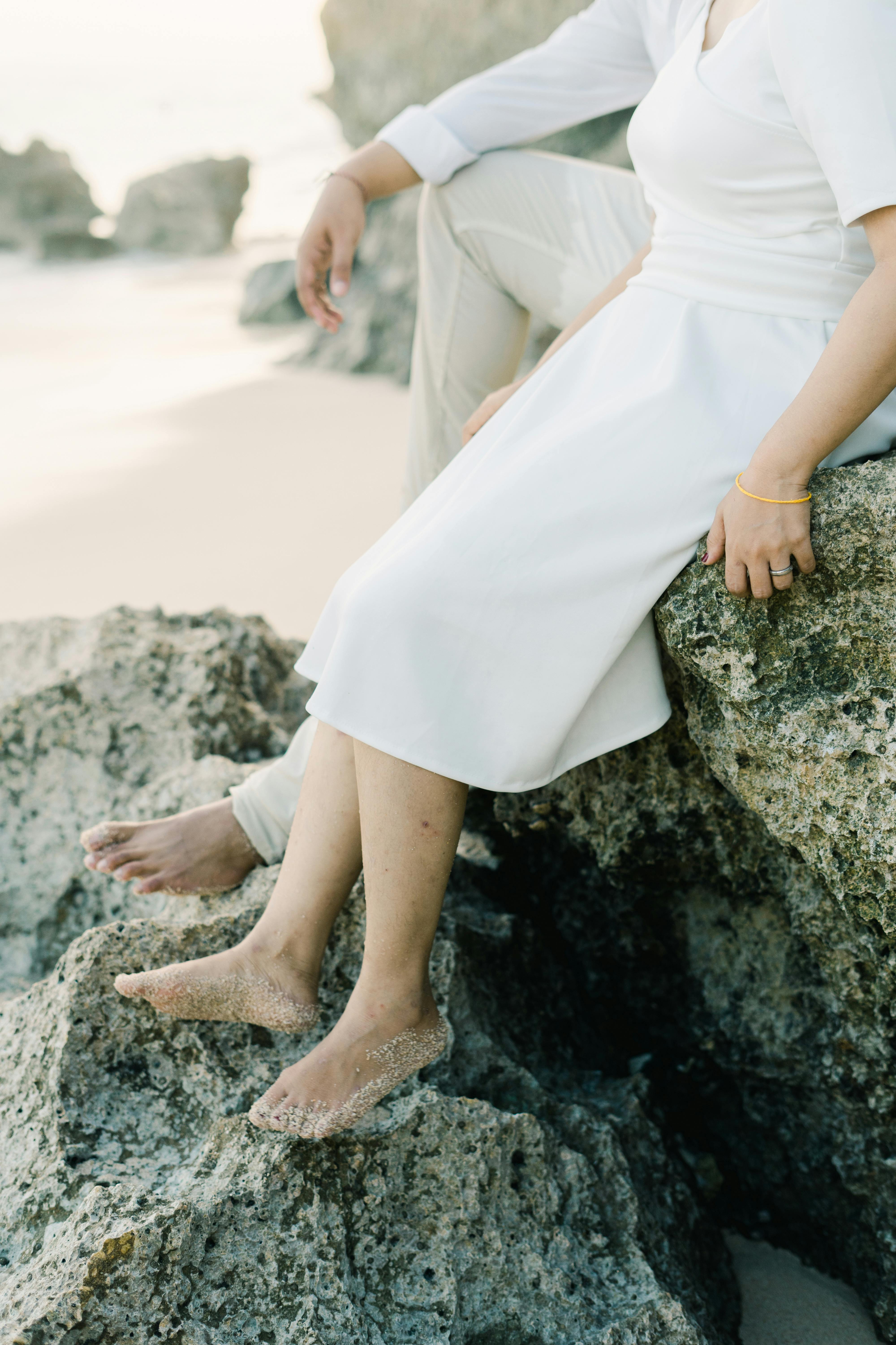 A couple sits barefoot on rocky beach terrain, showcasing leisure and romance.