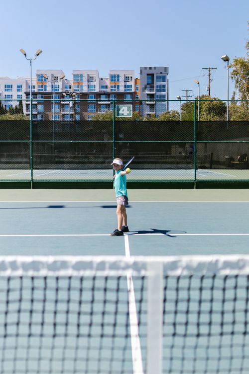 Free A young girl playing tennis on an outdoor court with a visible cityscape in the background. Stock Photo