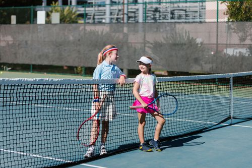 Free Two young girls in sportswear chatting at the tennis net during a break on an outdoor court. Stock Photo
