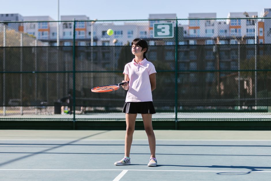 Girl playing tennis on sunny outdoor court, perfecting her serve during practice session.
