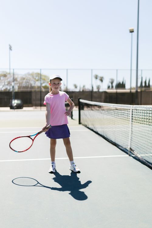Free A cheerful young girl in sports attire playing tennis on an outdoor court under a bright sky. Stock Photo