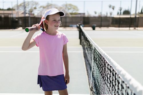 Free A cheerful young girl on a tennis court holding a racket, enjoying the sport outdoors. Stock Photo