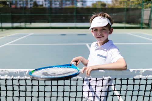 Free A smiling young boy in sportswear holding a tennis racket on a sunny outdoor court. Stock Photo