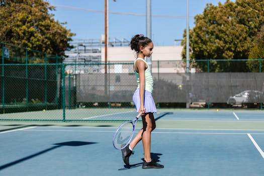 A girl wearing sportswear practices tennis on an outdoor court.