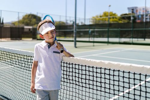 Free Child in tennis attire posing with a racket on an outdoor court. Stock Photo