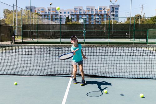 Free A young girl in sportswear practices tennis on a sunny outdoor court with multiple tennis balls around. Stock Photo