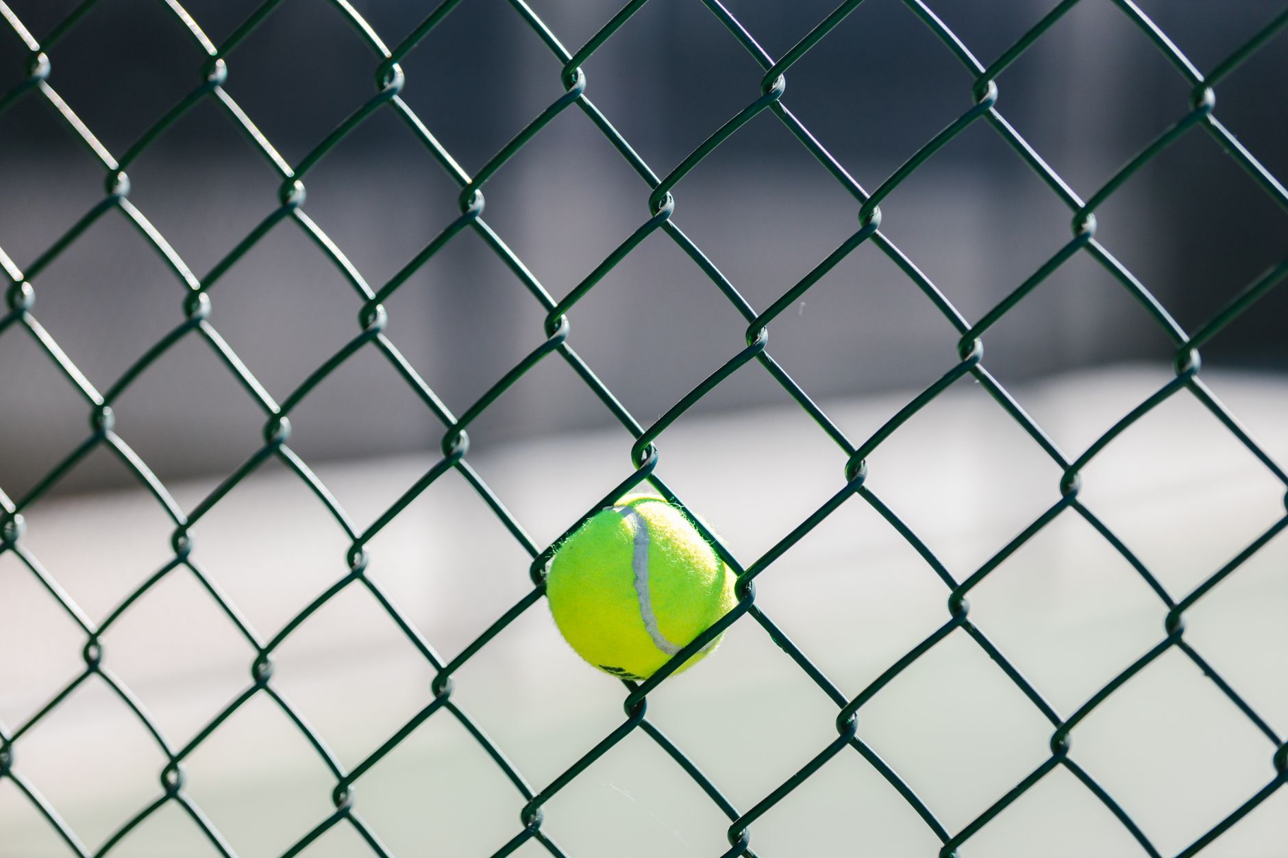 Close-up of a tennis ball caught in a chain-link fence outdoors.