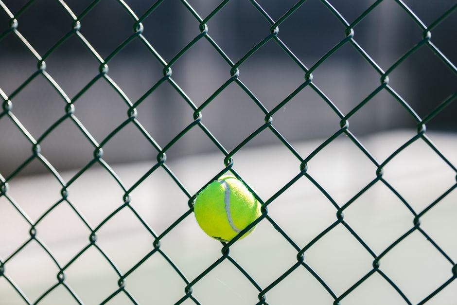Close-up of a tennis ball caught in a chain-link fence outdoors.