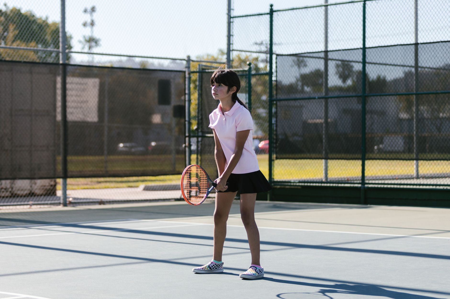 A young girl in sportswear practicing tennis on an outdoor court during the day.