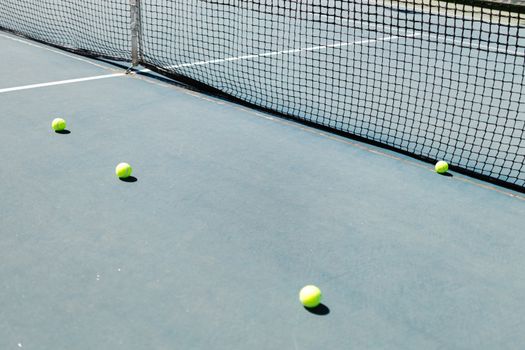 A tennis court featuring a net and several tennis balls lying on the ground, well-lit by sunlight.