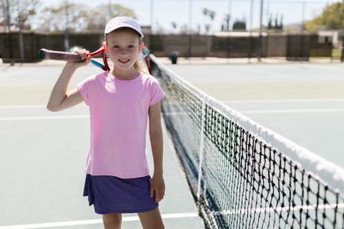 Free Smiling young girl holding a tennis racket on an outdoor tennis court in daylight. Stock Photo