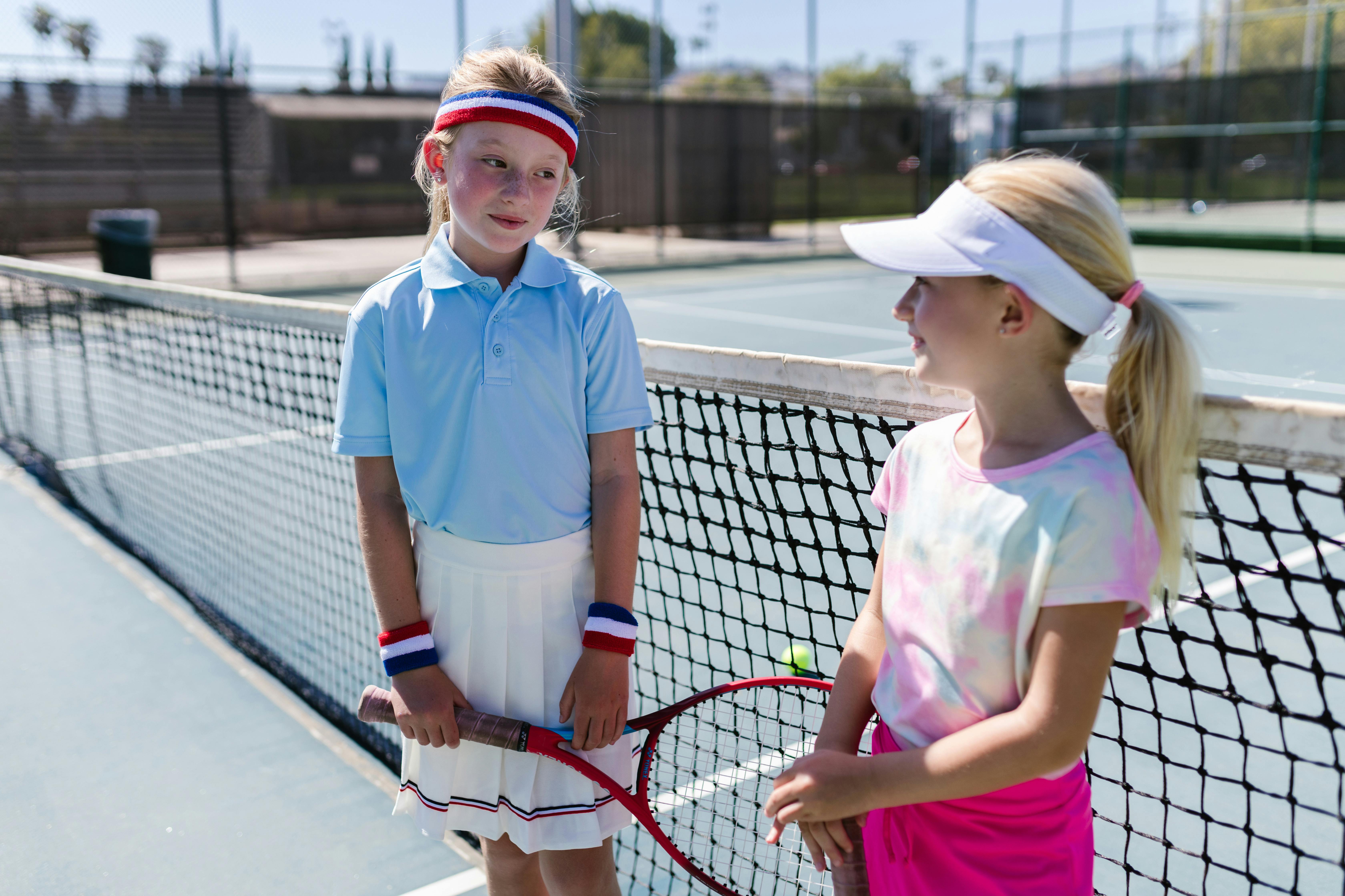 girls wearing sportswear standing by the tennis net