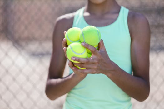 Close-up of a person holding multiple tennis balls on a sunny day at the tennis court.