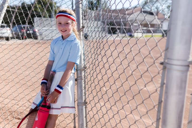 Smiling junior player with a headband by the court fence