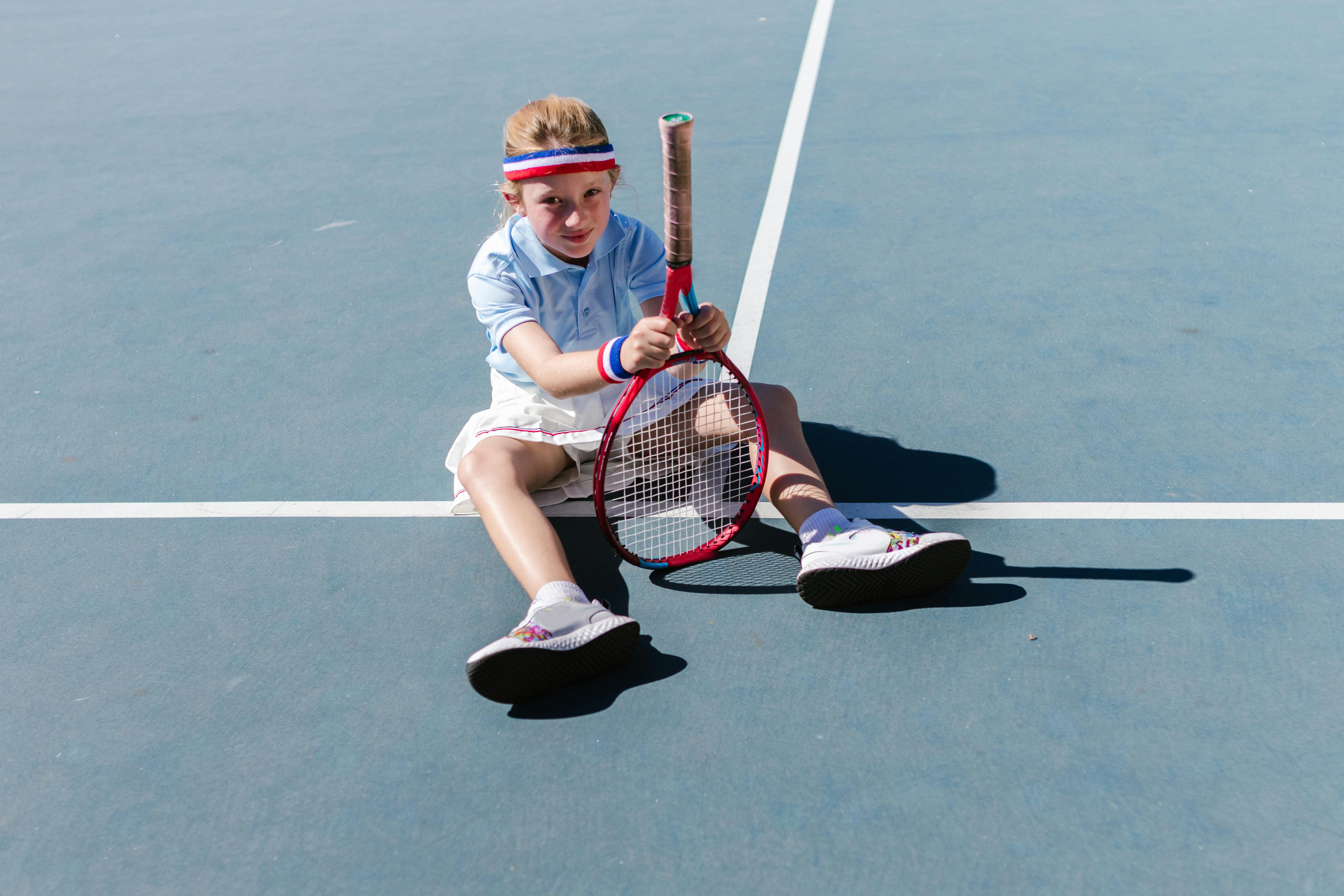 girl sitting on a tennis court while holding her tennis racket