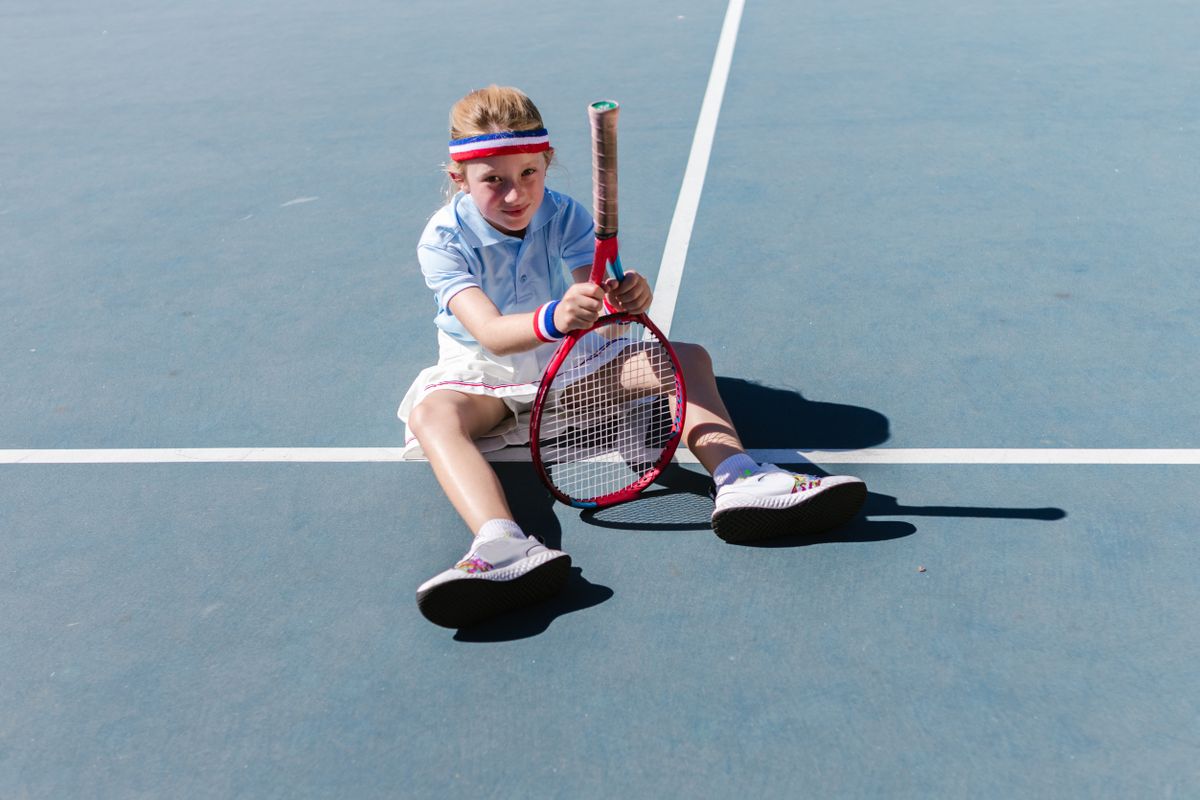 Young boy sitting on the court holding his racket