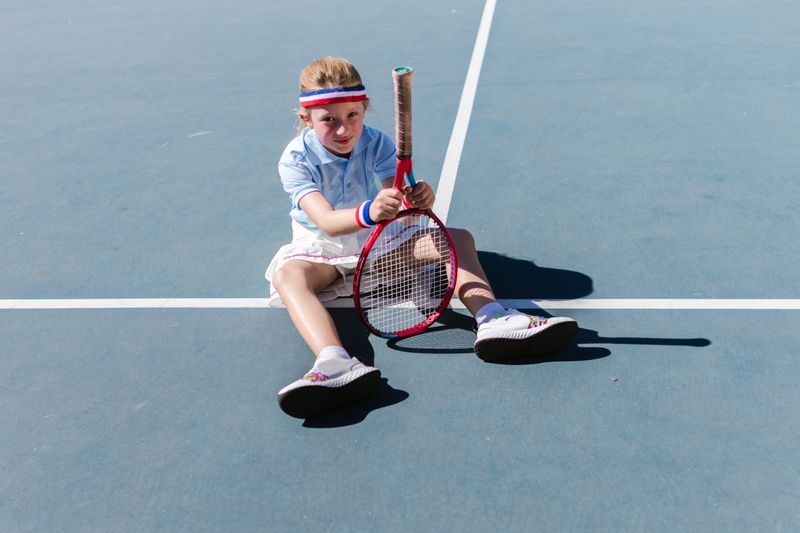 Young boy sitting on the court holding his racket