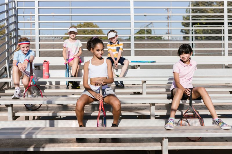 Group of junior players resting on the bleachers with rackets