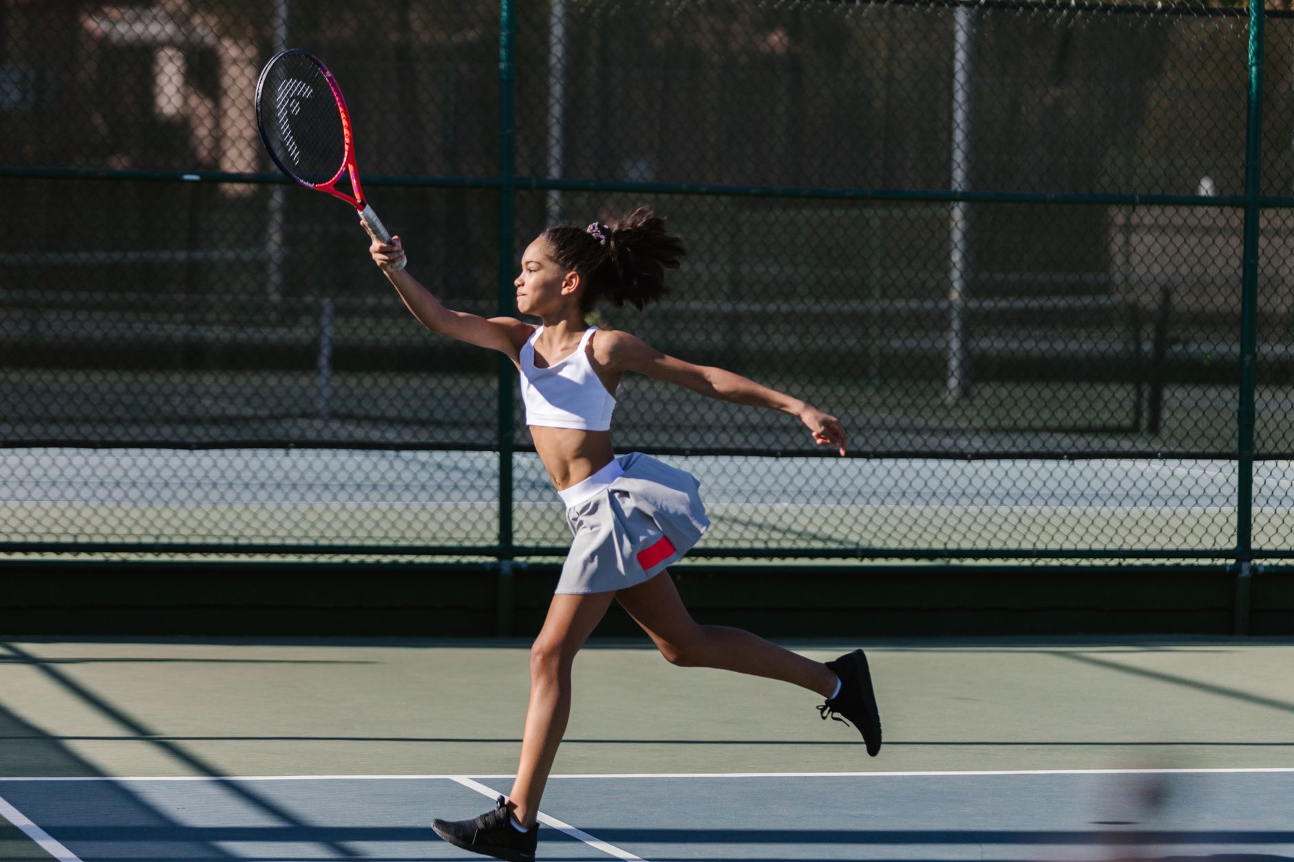 Dynamic shot of a teen girl playing tennis outdoors, showcasing athletic movement and sportswear.