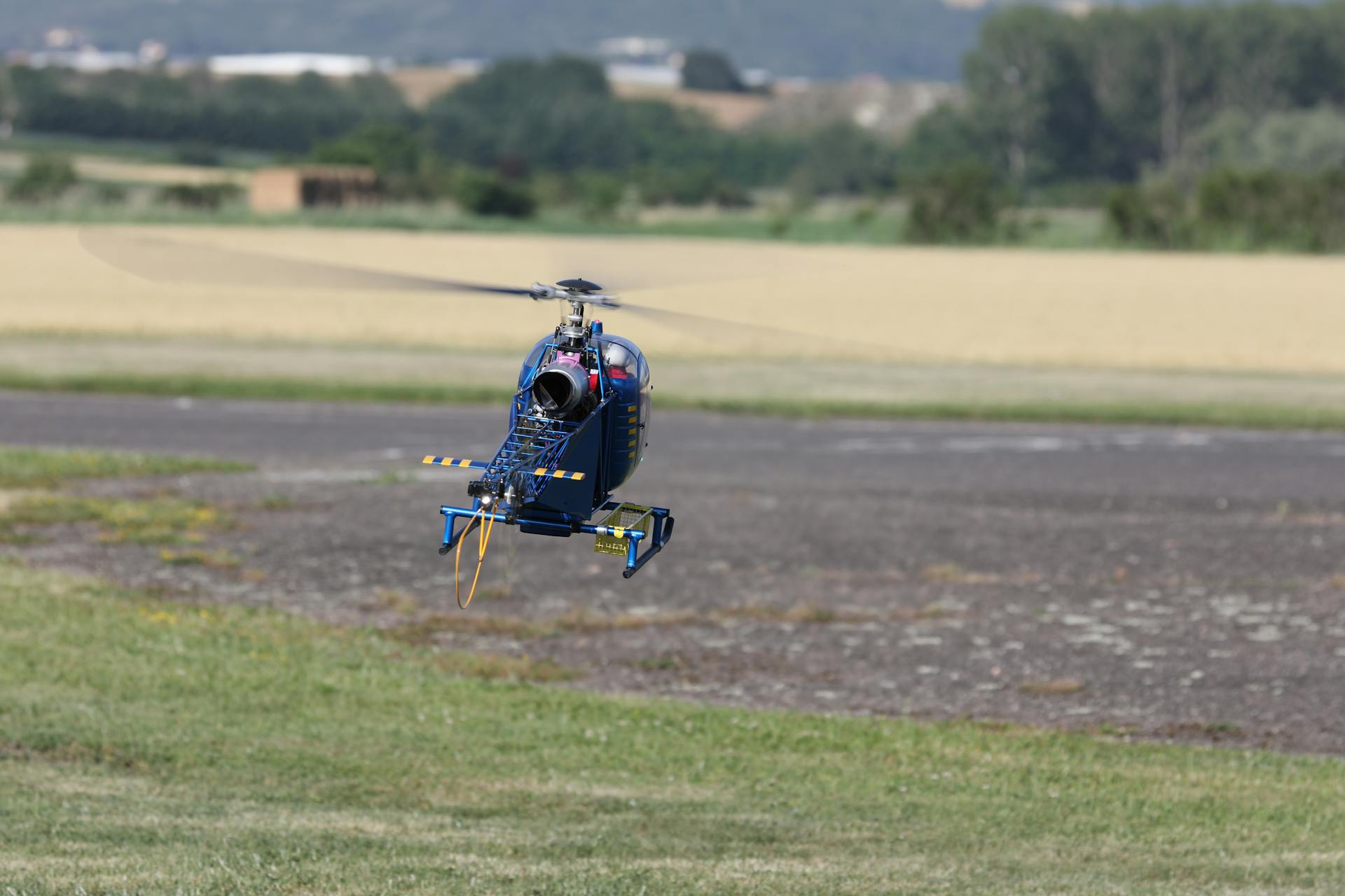 A remote-controlled helicopter flying over a field on a bright day.