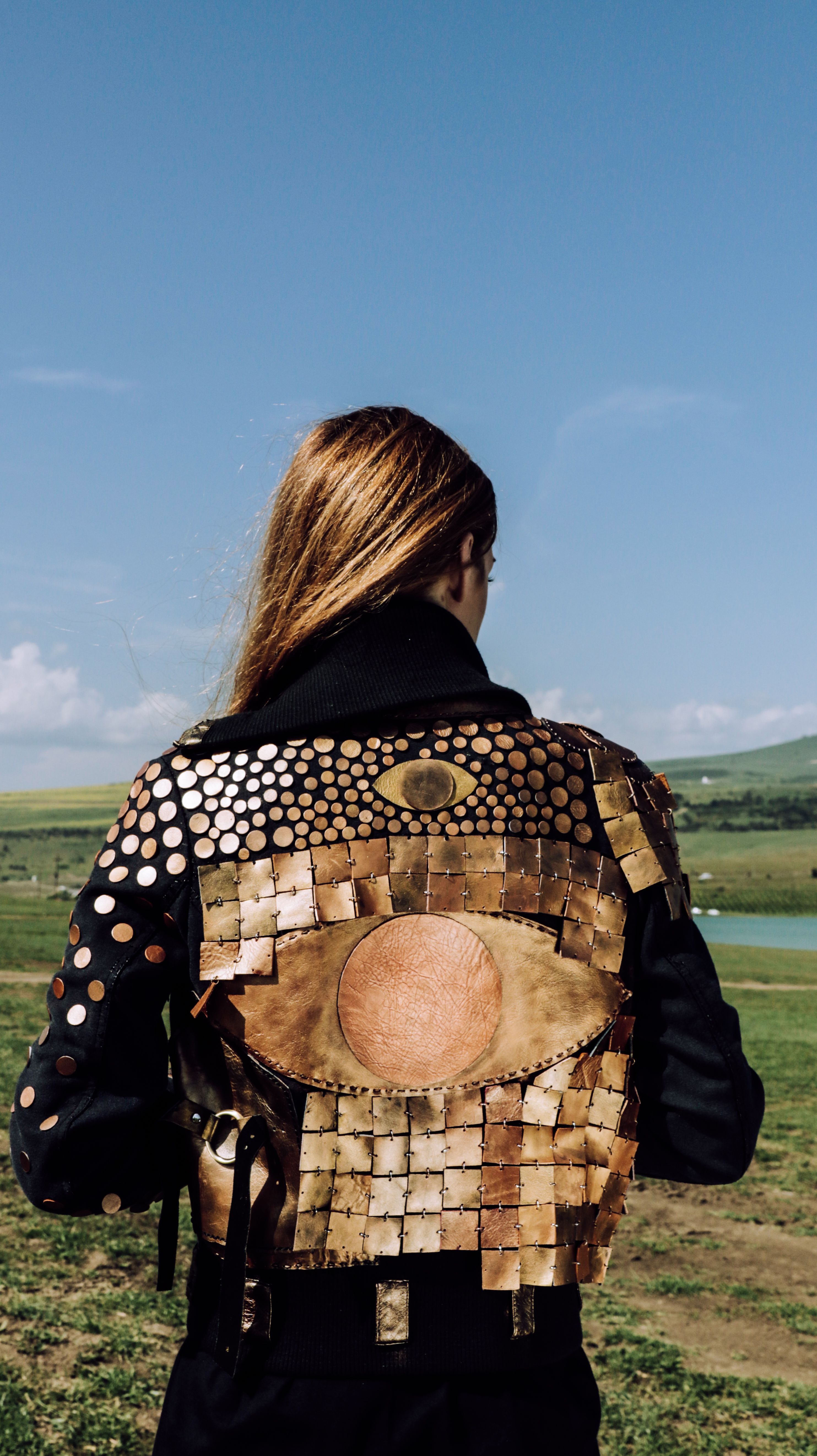Stylish jacket with metallic designs worn by person in countryside setting under blue sky.