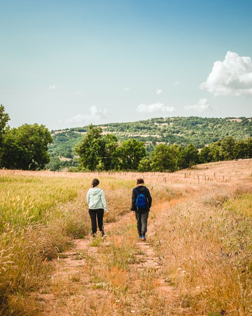 Free A couple walking on a picturesque trail surrounded by fields, hills, and a clear sky. Stock Photo