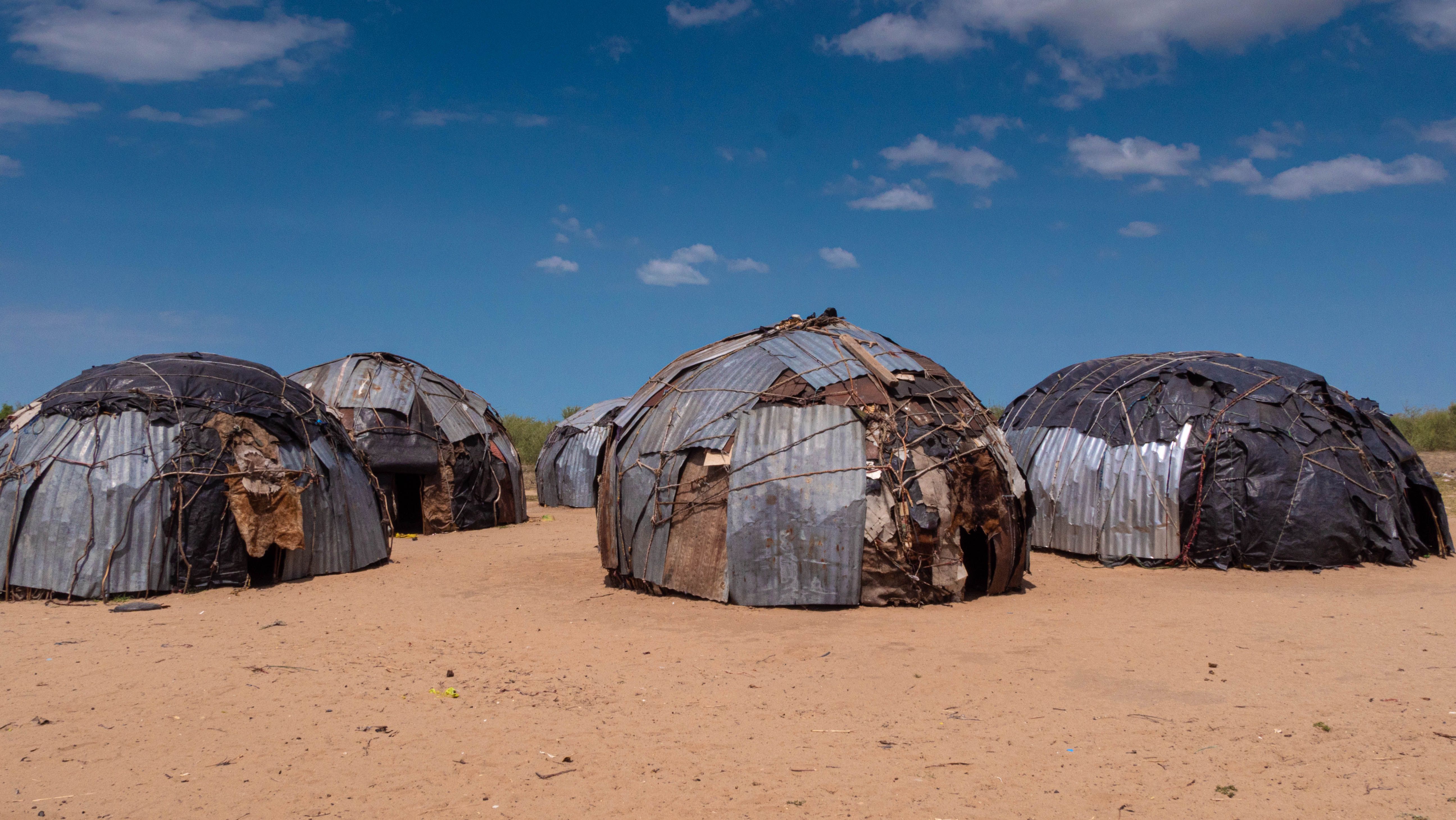 Traditional circular huts in a rural African village beneath a blue sky.