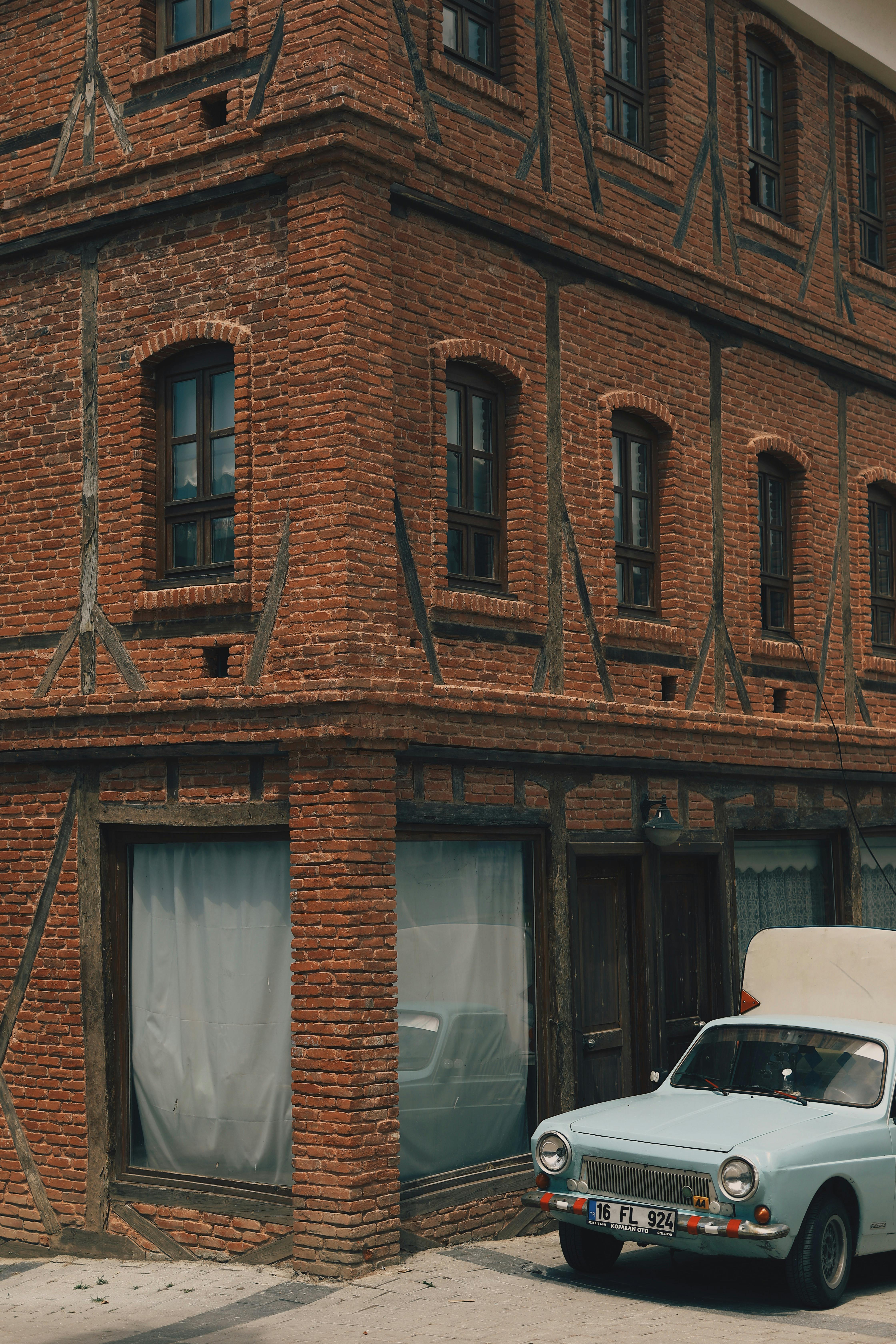 Free A classic car parked by a vintage red brick building corner showcasing architectural details. Stock Photo