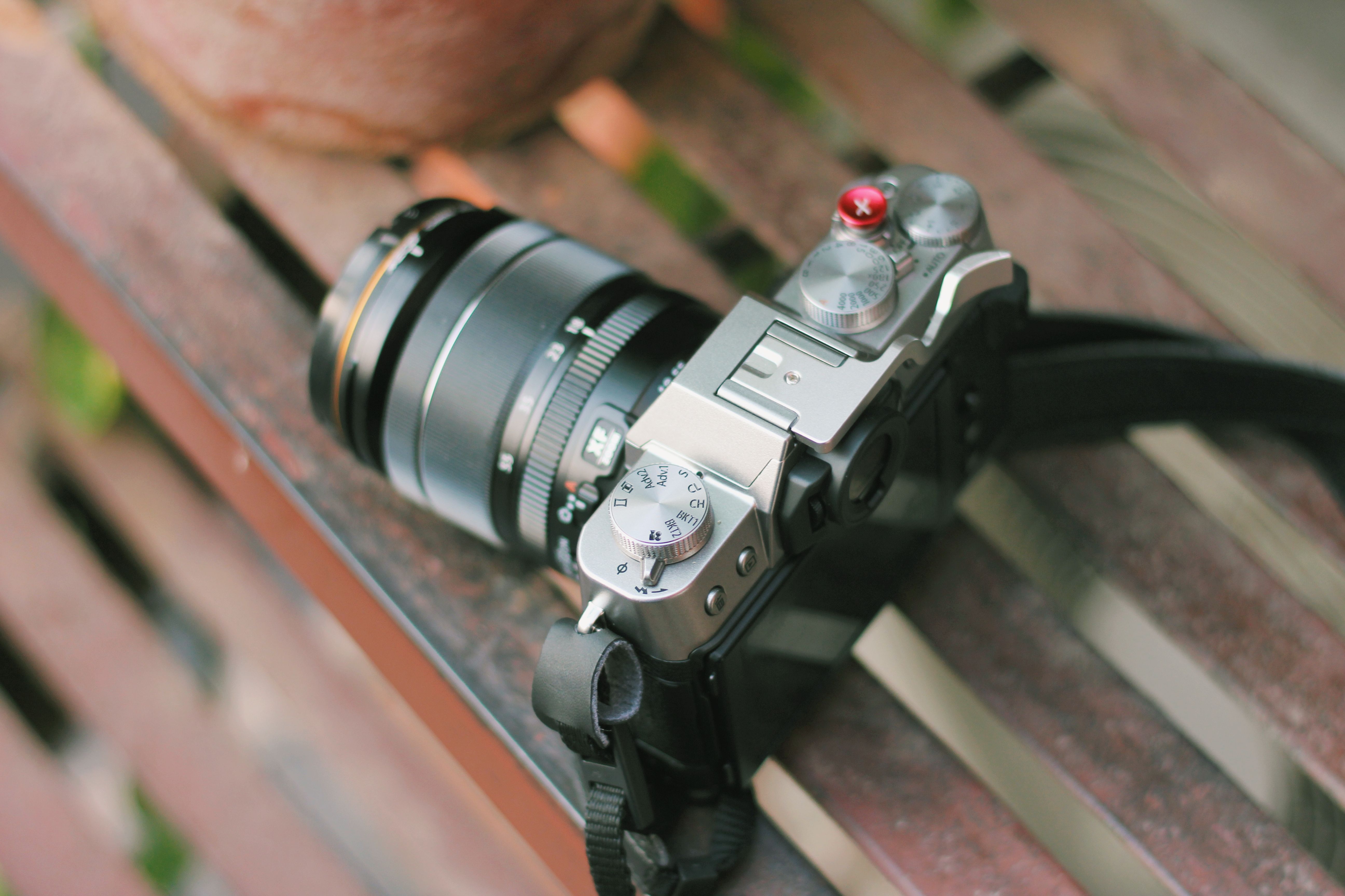 Close-up shot of a retro-style camera with a lens on a wooden bench outdoors.