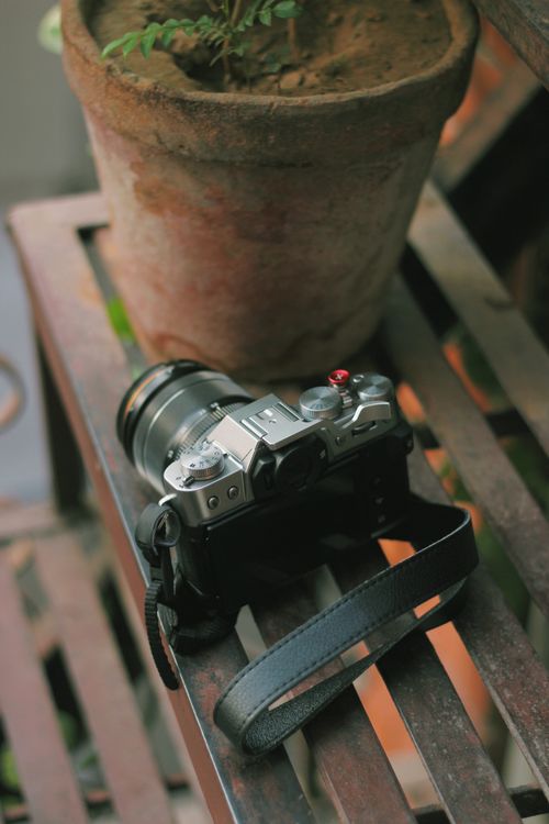 Free A camera lies on a metal bench beside a clay pot with a plant, creating an artful and rustic scene. Stock Photo