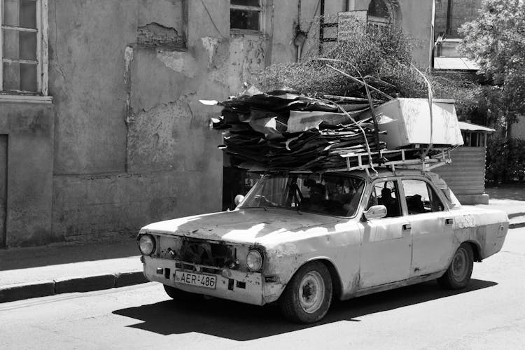 A Person Driving A Shabby Car Carrying Metal Scraps