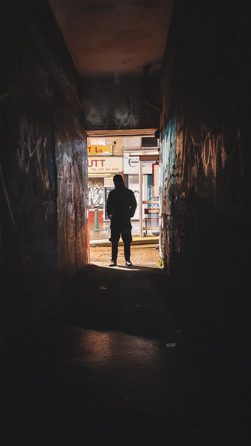 Free Dramatic silhouette of a man standing in a dimly lit urban alleyway with graffiti. Stock Photo