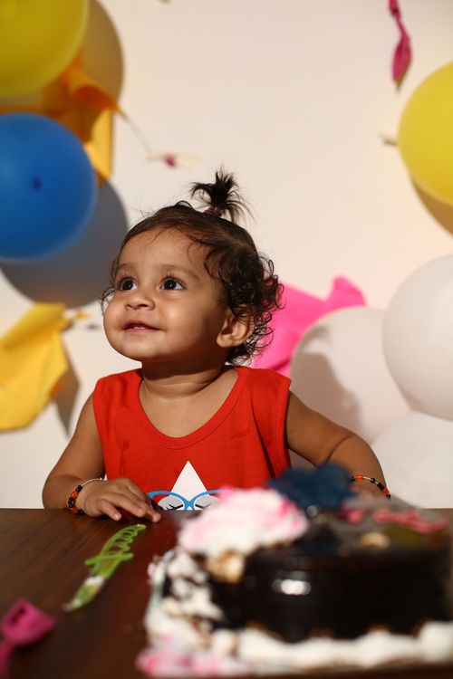 Free Charming toddler in red outfit enjoying a birthday celebration with colorful balloons and cake. Stock Photo