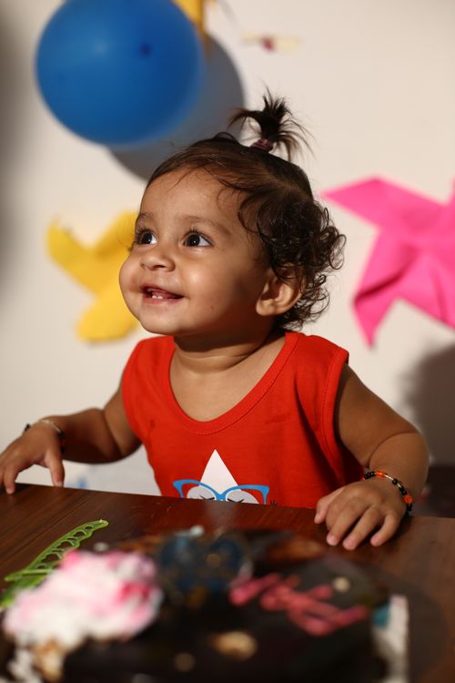 Free Cute baby smiling at a colorful birthday party with balloons and cake indoors. Stock Photo