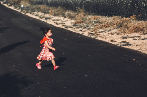 Free A young girl in a red striped dress walks confidently along a rural road on a sunny day. Stock Photo