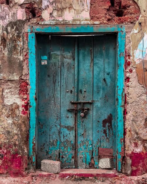 Free A rustic blue wooden door set in a weathered, colorful wall with peeling paint. Stock Photo