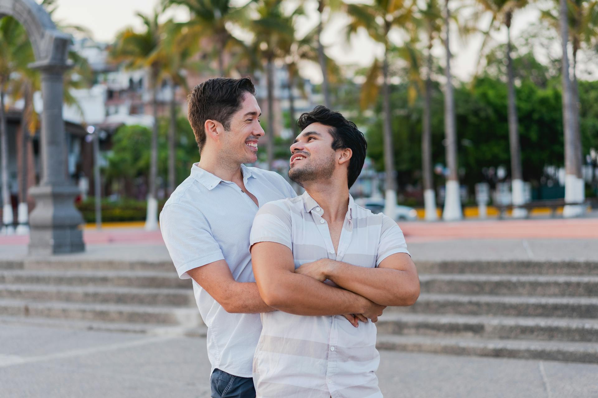 Smiling gay couple embracing outdoors, conveying love and happiness on a sunny day.